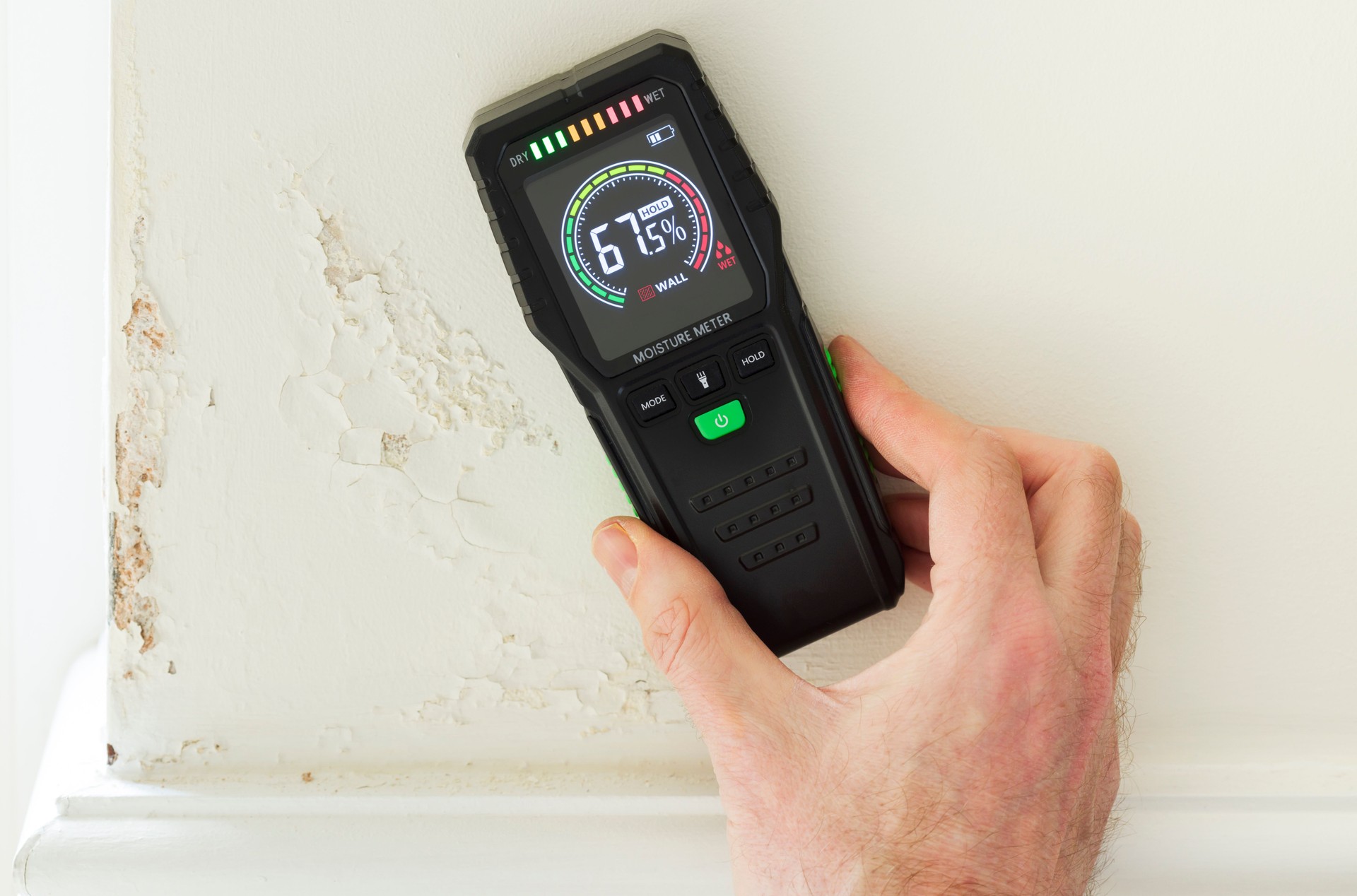 Moisture meter against a wall with rising damp, UK home interior