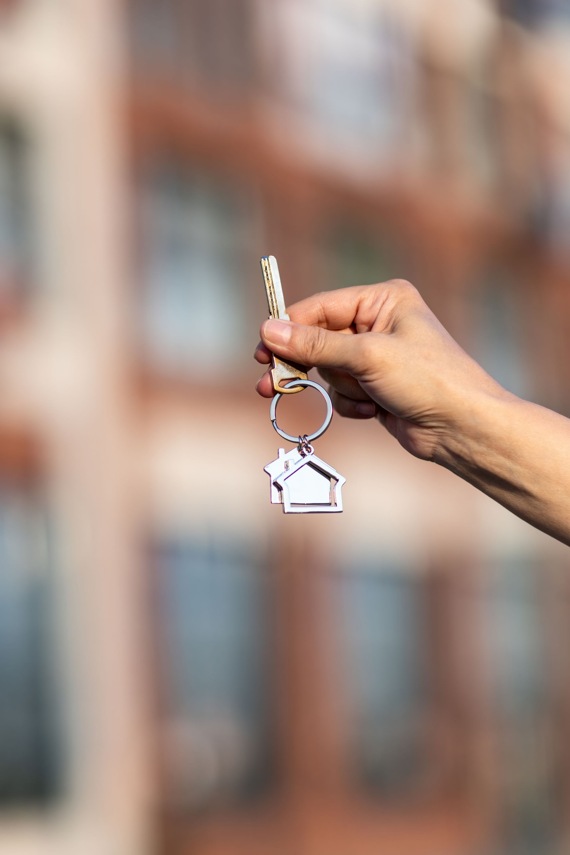 Hand holding key from new flat against residential apartment building façade.